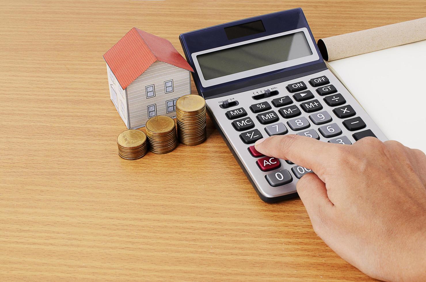 Calculadora de mano con pila de monedas y casa de papel para concepto de préstamos hipotecarios foto