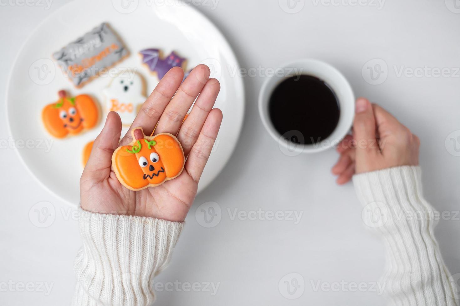 mano de mujer sosteniendo una divertida galleta de halloween durante el consumo de café. feliz día de halloween, truco o amenaza, hola octubre, otoño otoño, tradicional, concepto de fiesta y vacaciones foto