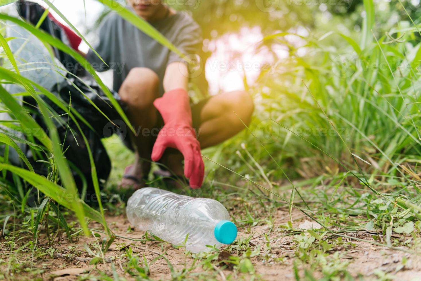 La mano del hombre del muchacho recoge la botella plástica en el bosque. concepto de medio ambiente. foto