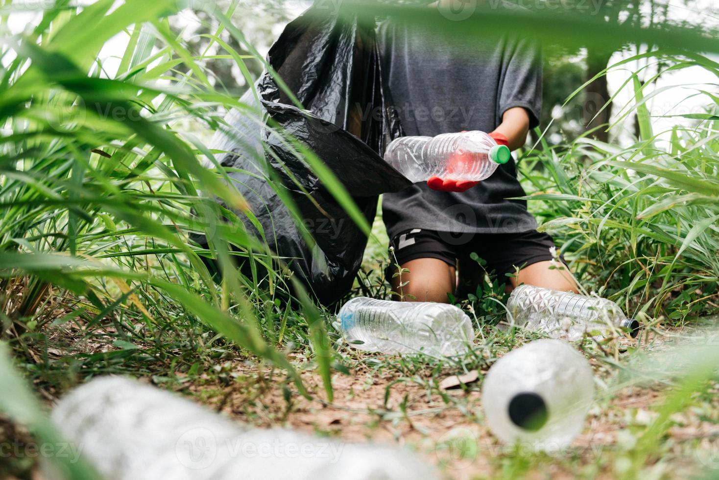 La mano del hombre del muchacho recoge la botella plástica en el bosque. concepto de medio ambiente. foto