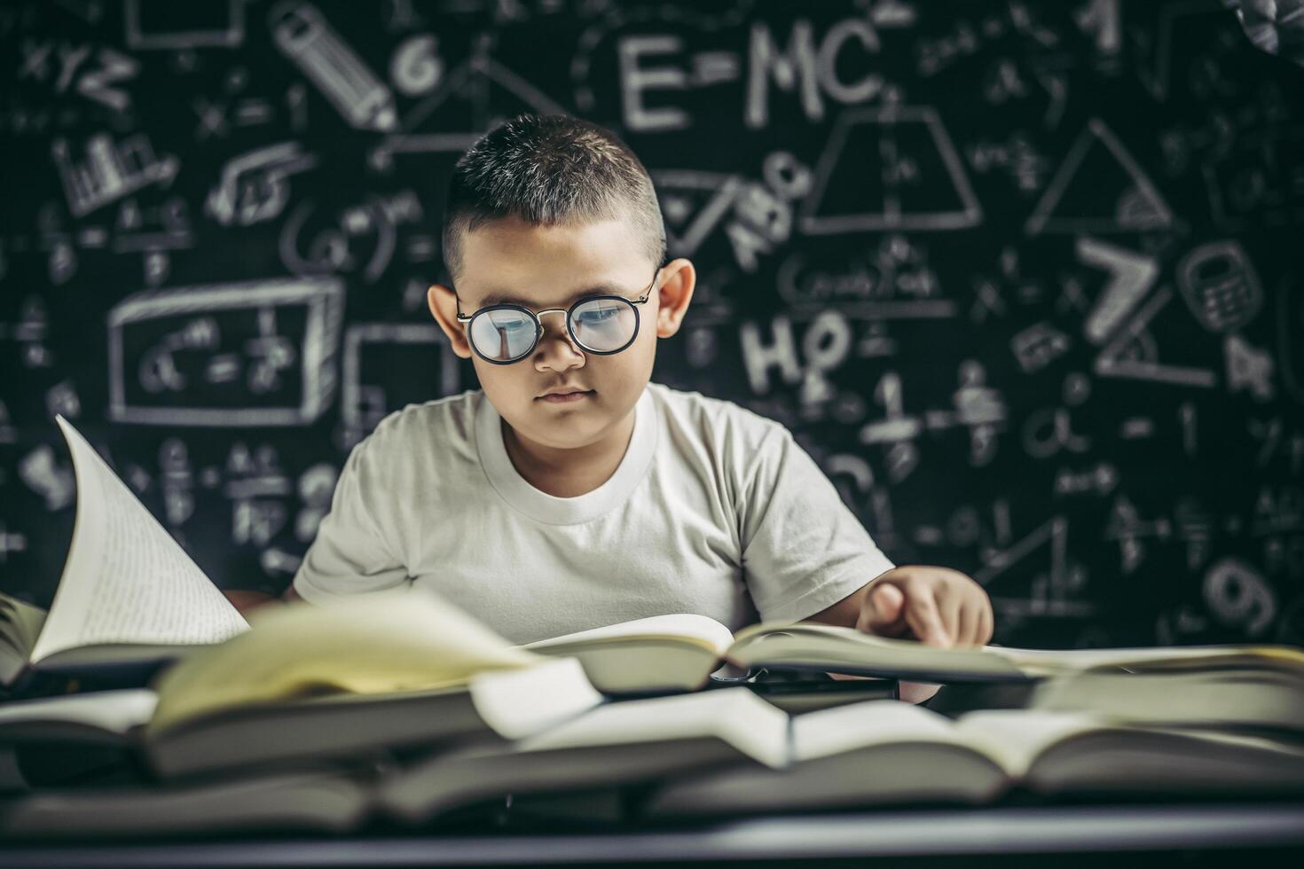 A boy with glasses sitting in the classroom reading photo