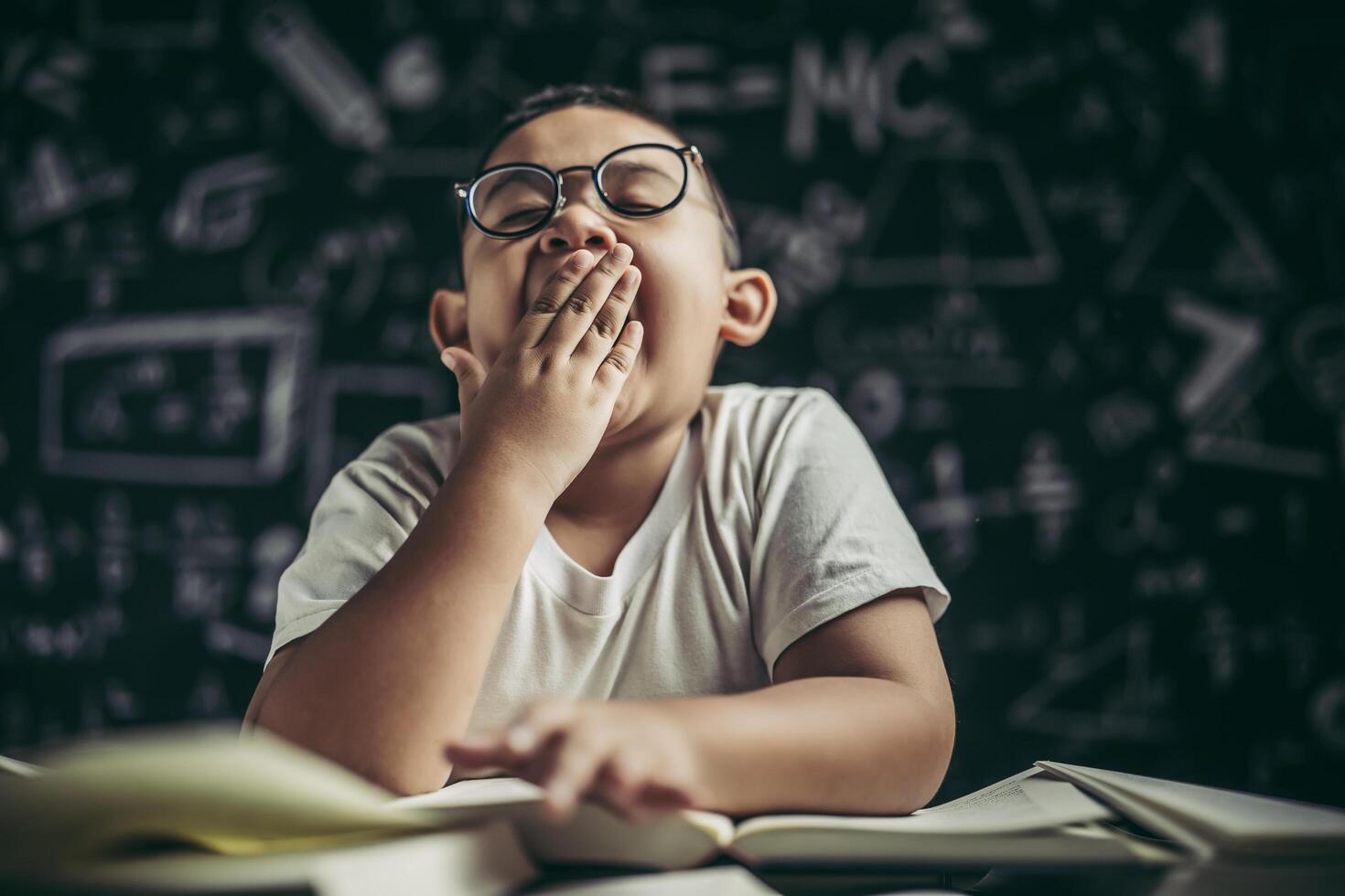 un niño con gafas estudiando y somnoliento. foto