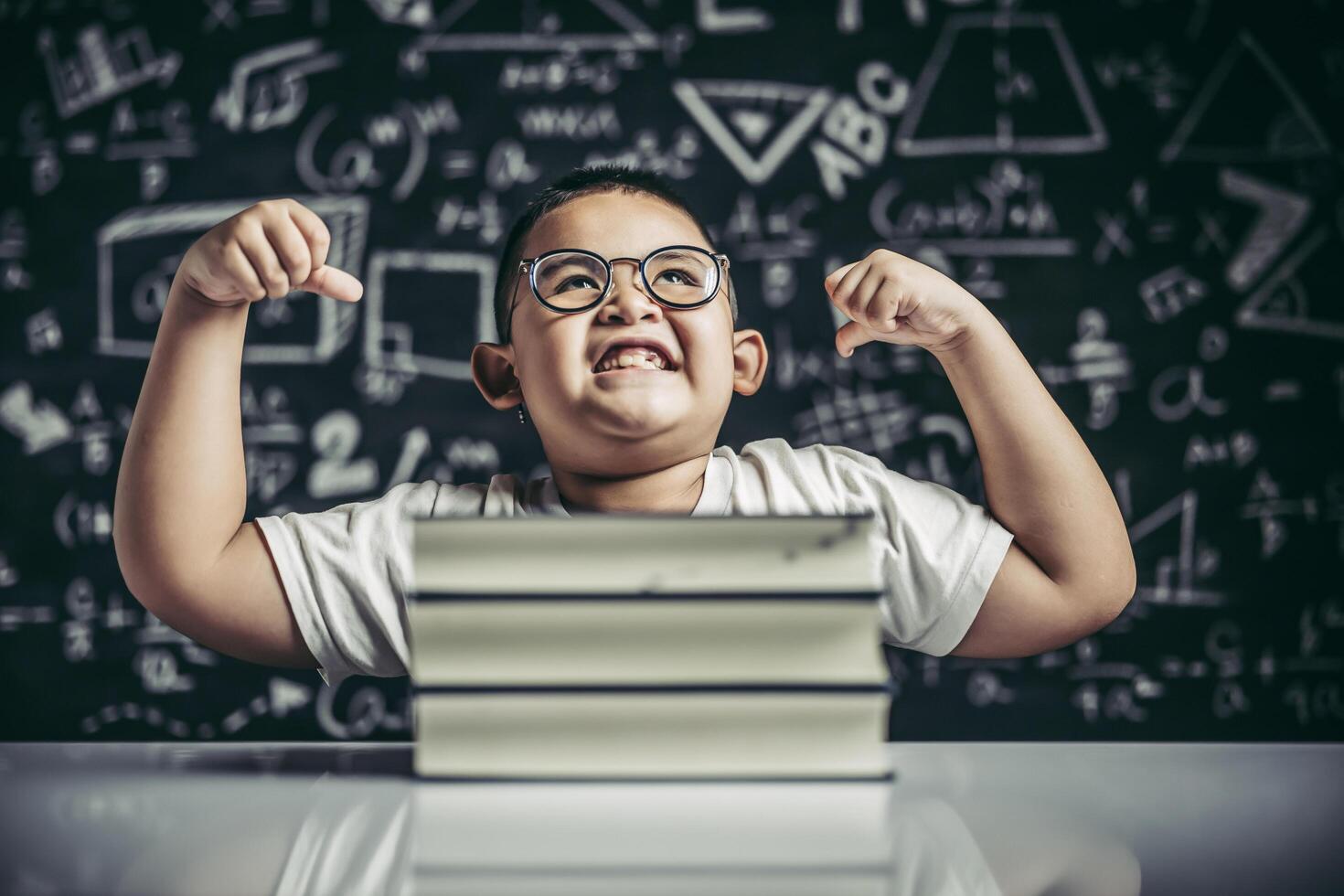 A boy with glasses sitting in the study and with both arms perpendicular photo