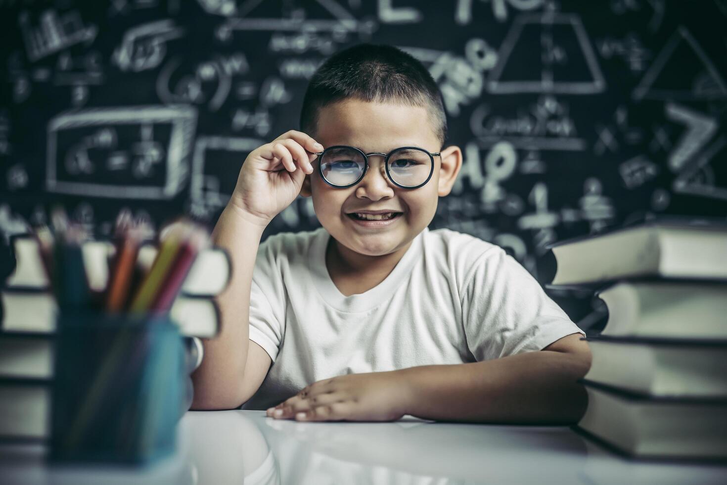 Boy studying and holding glasses leg in classroom. photo