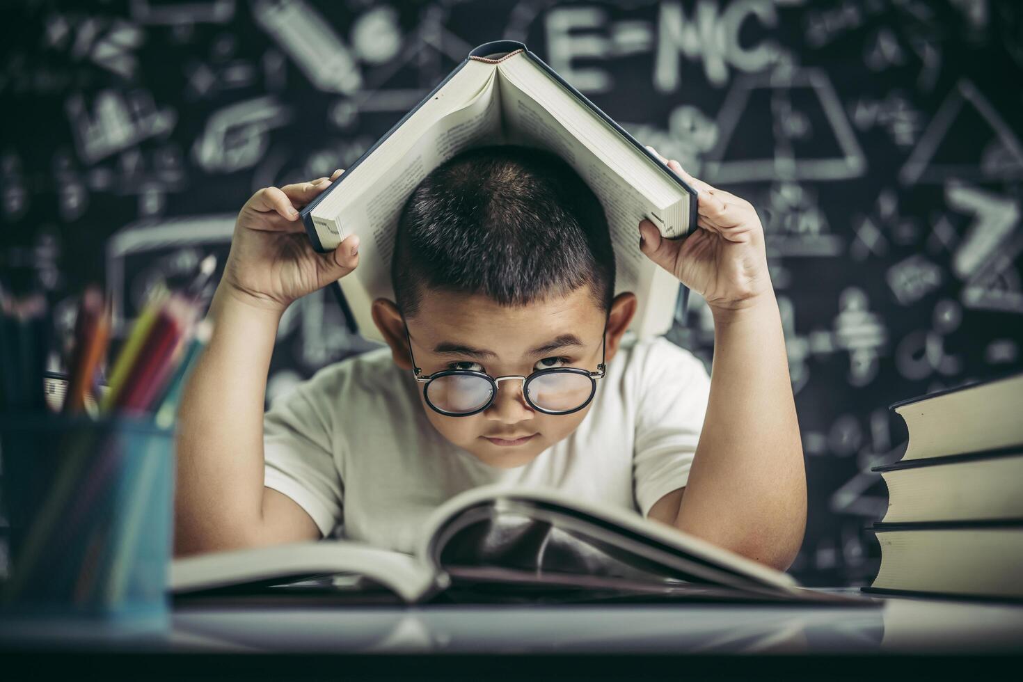 A boy with glasses studied and put a book on his head in the classroom. photo