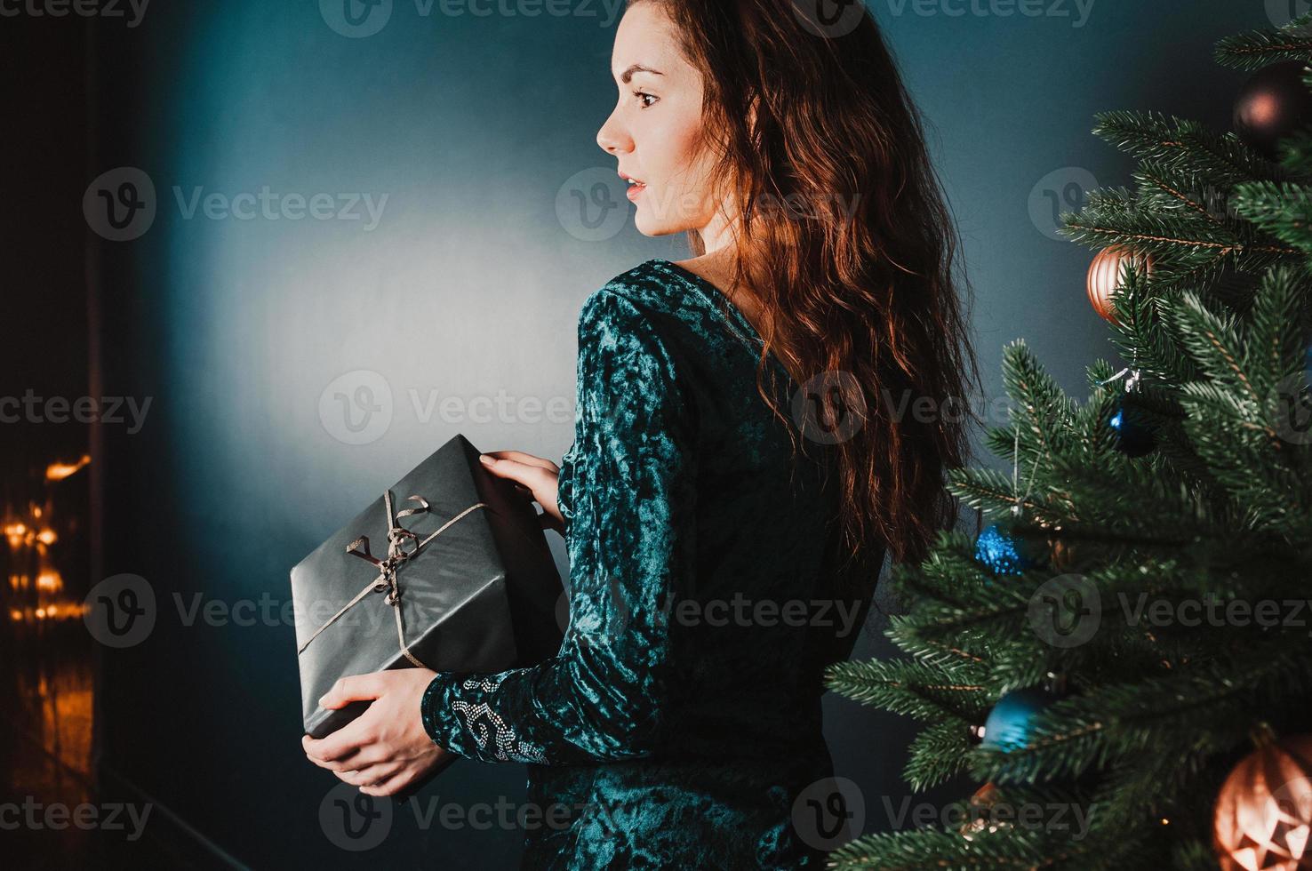 niña bonita con caja de regalo cerca del árbol de navidad, sorprendido foto