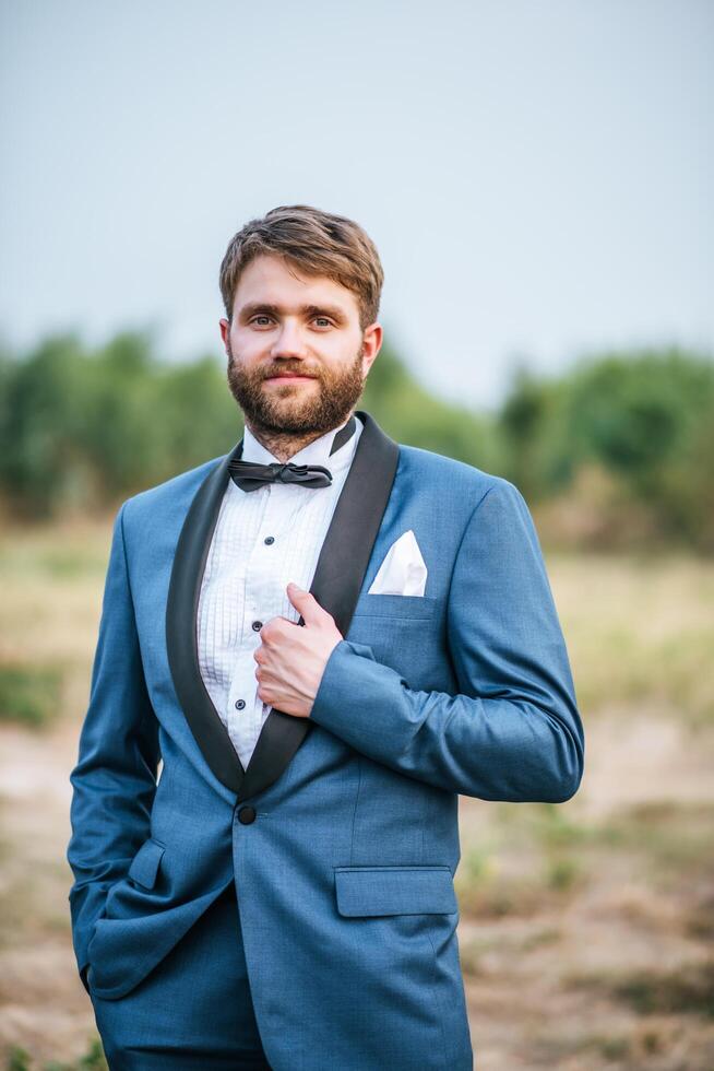 Handsome groom in wedding suit posting in the park photo