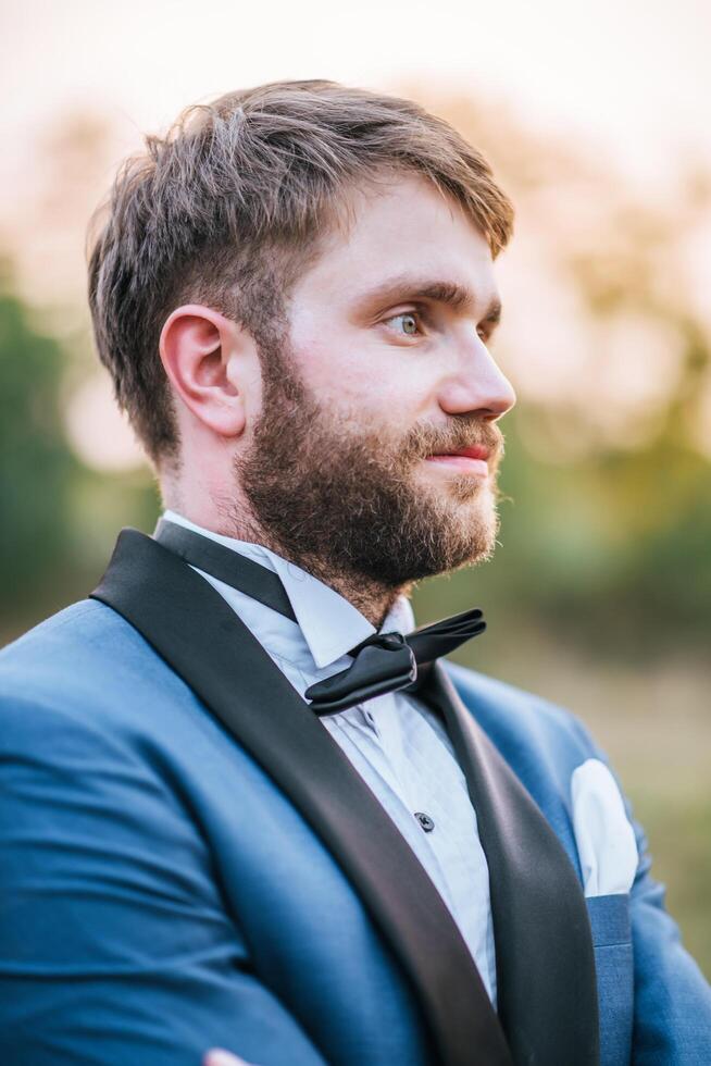 Guapo novio en traje de boda publicar en el parque foto