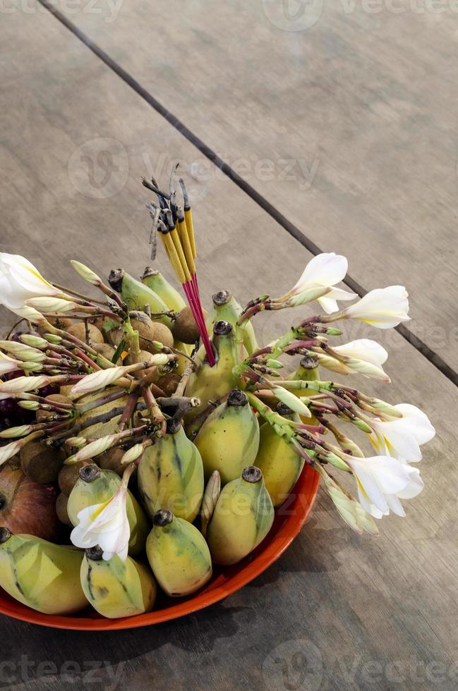 Tazón de ofrenda budista con incienso detalle de flores y frutas foto