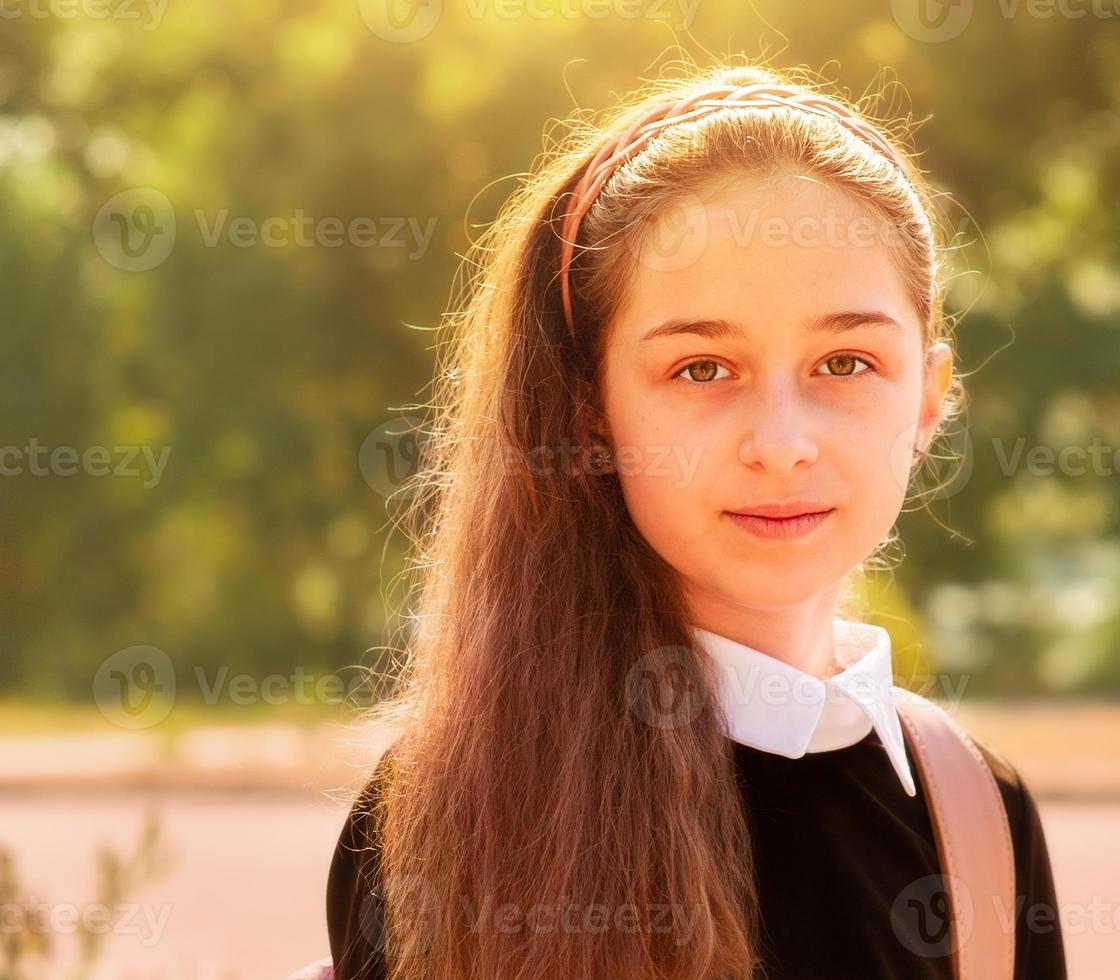 Schoolgirl in school clothes in nature on a background of leaves. Girl 11 years old. photo