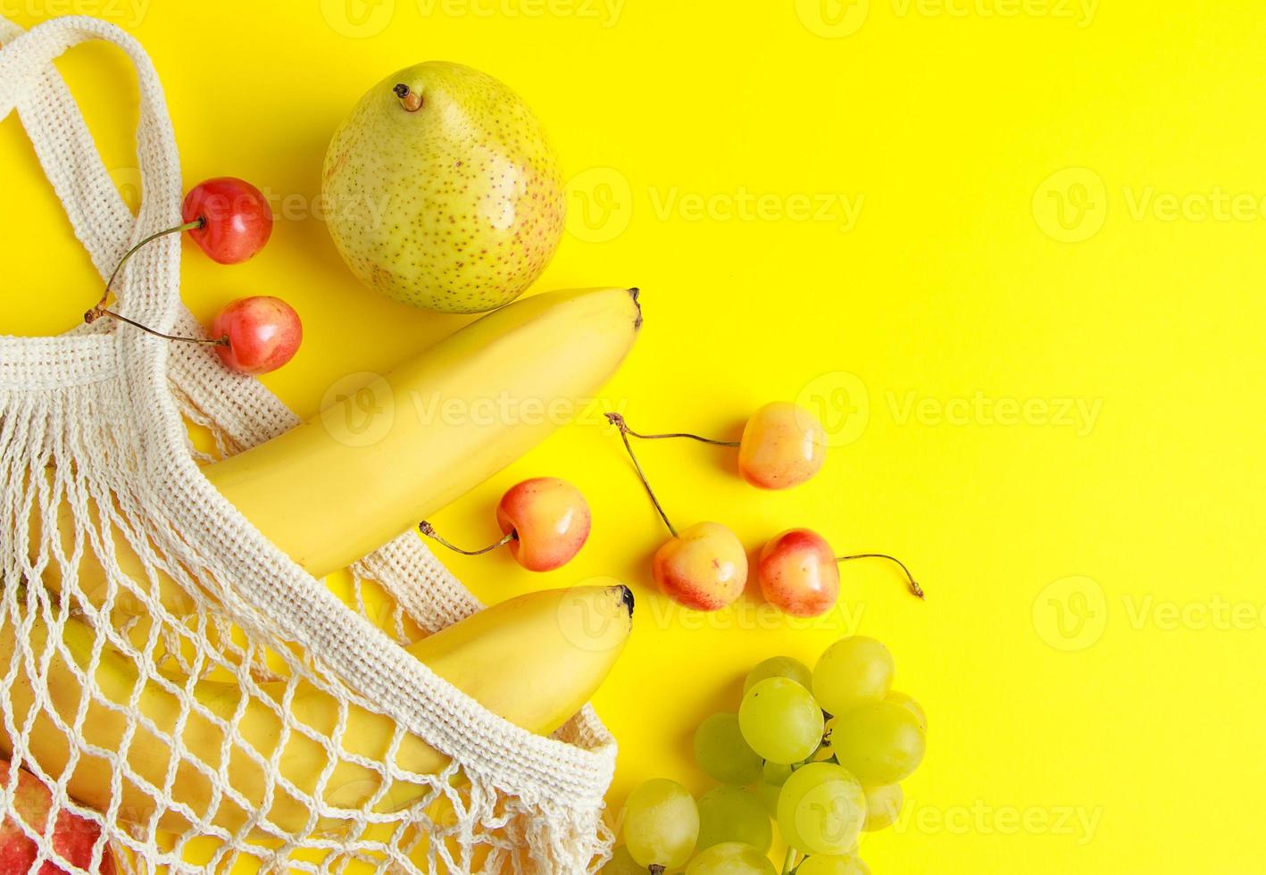 Eco-friendly cotton shopping bag. Ripe fruits in mesh bag on yellow background. Organic vegan food. Sustainable lifestyle and zero waste concept. photo