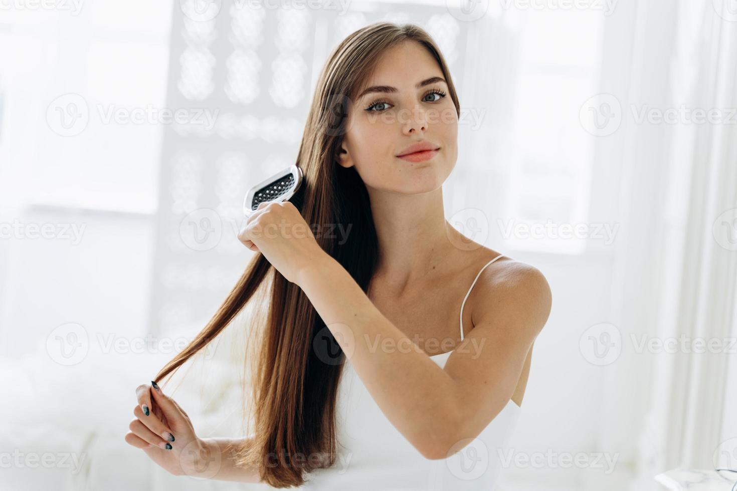 Brushing hair. Portrait of young woman brushing straight natural hair with comb. Waist up of girl combing beautiful long healthy hair with hairbrush. Hair care and beauty concept photo