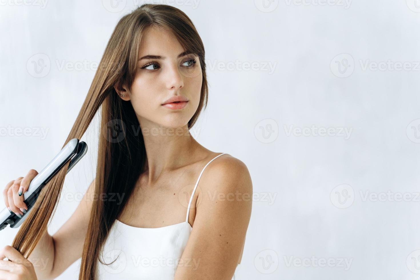 Close up retrato de mujer joven tranquila feliz disfrutando de alisarse el cabello con plancha y mirando a otro lado con una mirada de ensueño. concepto de cabello sano foto