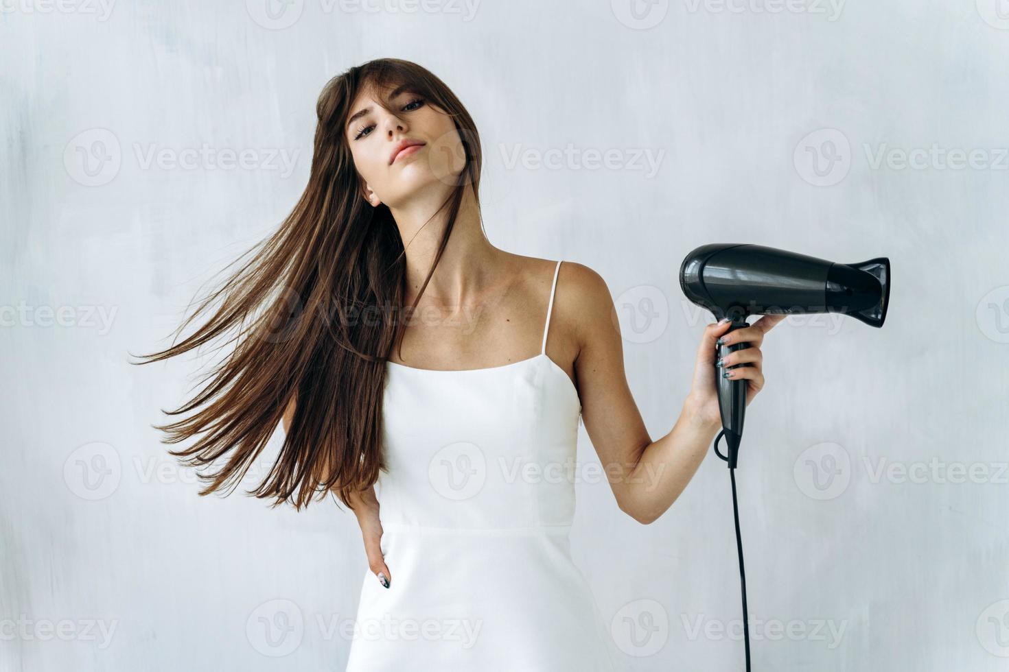 Portrait view of the sensual woman drying her hair in bathroom. Calm young woman blow drying hair in bathroom while feeling satisfied emotions. Stock photo