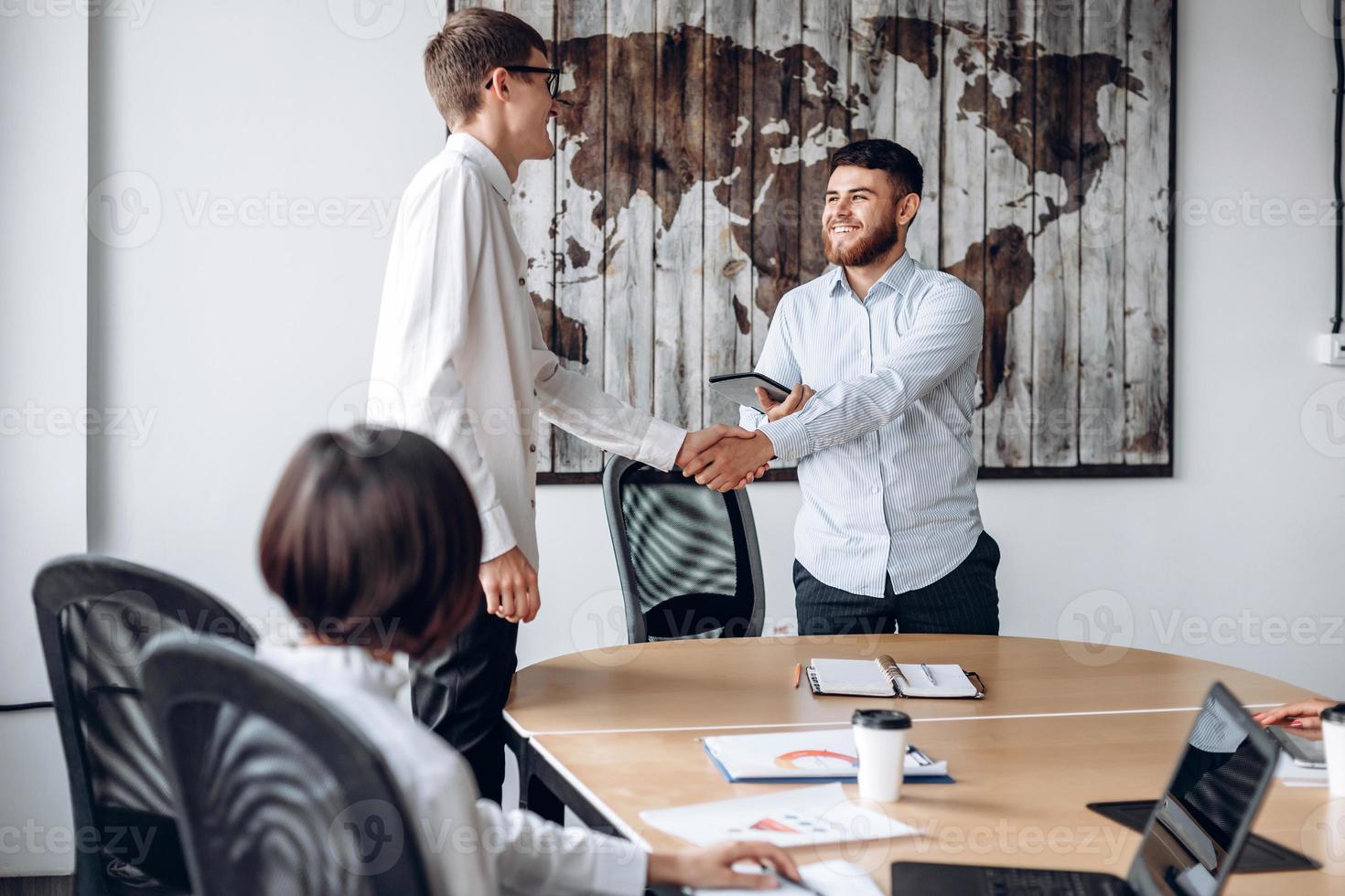 A smiling bearded boy shakes his colleague's hand in the office photo