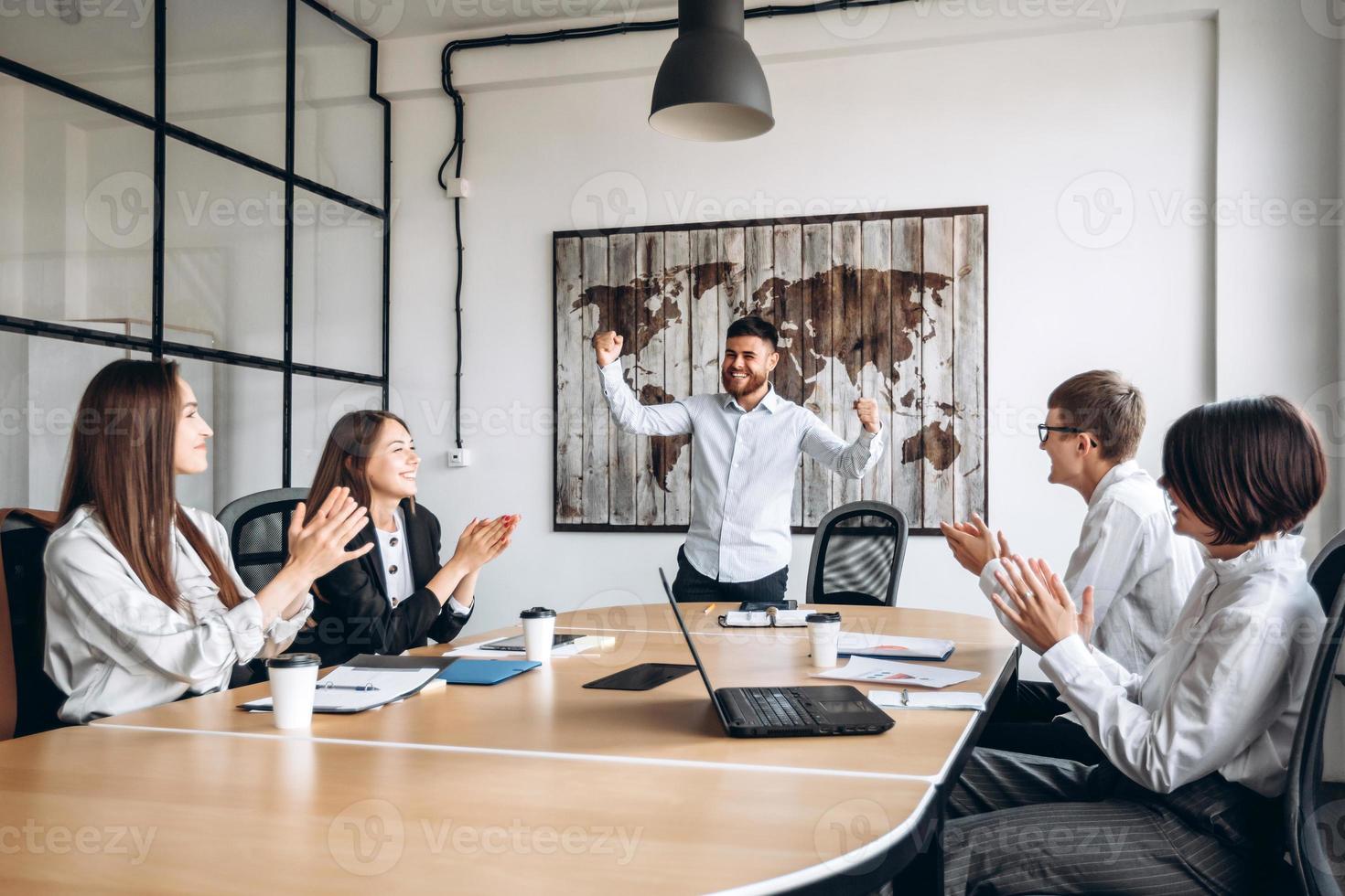 Un hombre barbudo joven guapo feliz hace gesto de ganador en la oficina de negocios. se regocija con sus colegas foto