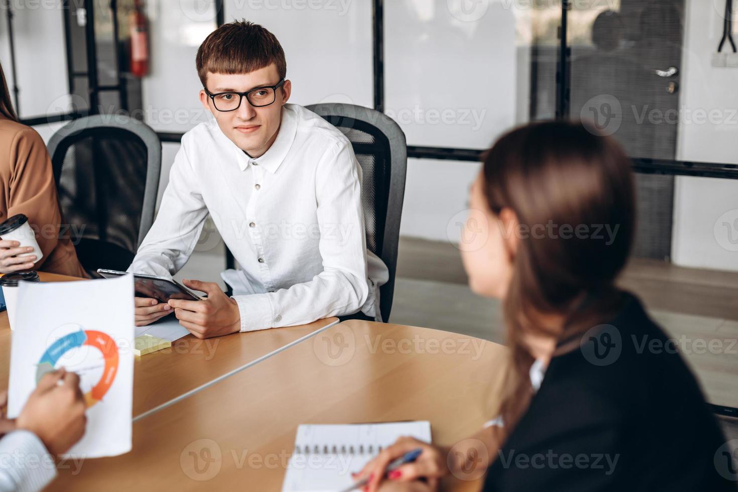 Joven con gafas en una reunión de negocios, escuchando atentamente a su colega foto