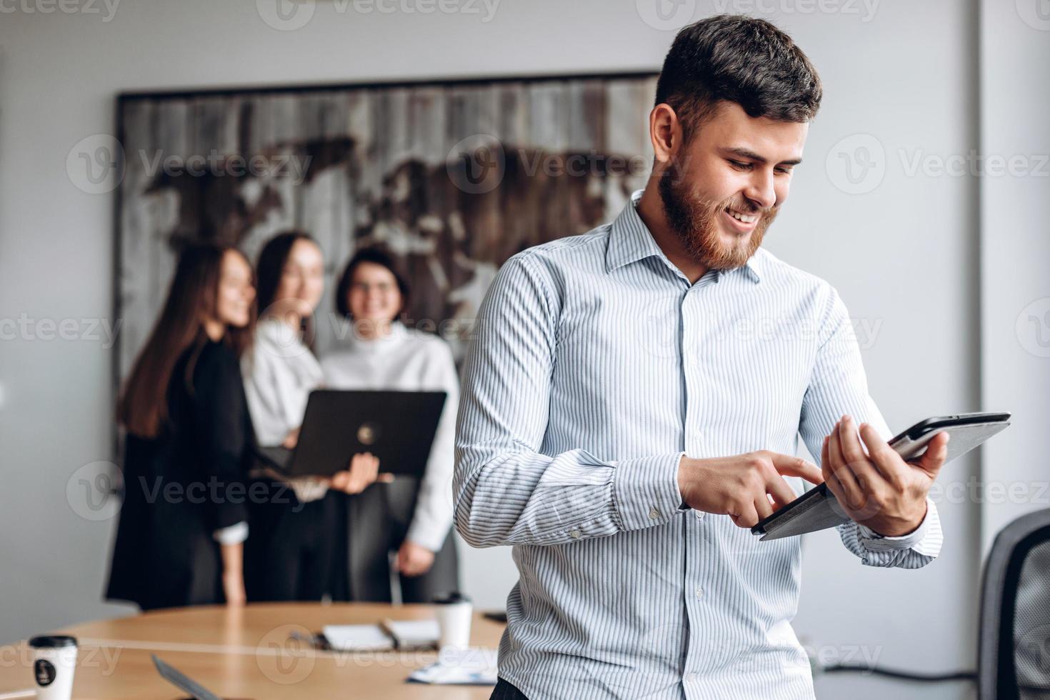 A smiling, attractive, young guy with a beard works on a tablet in the office. photo