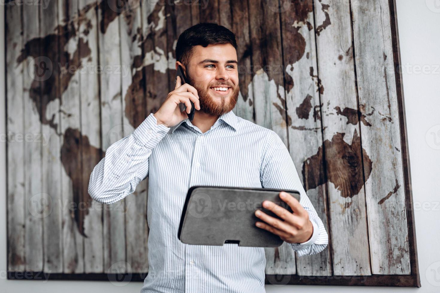 Handsome busy businessman talking on the phone and looking at important document on tablet. photo