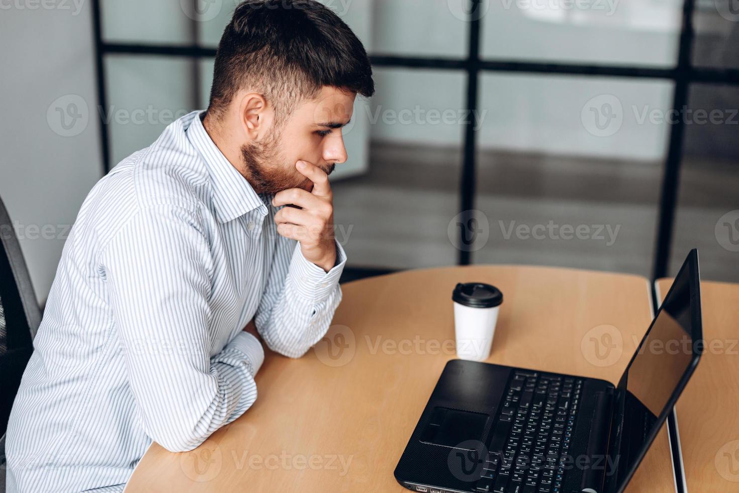 un hombre barbudo con una camisa piensa intensamente mientras trabaja en la oficina foto