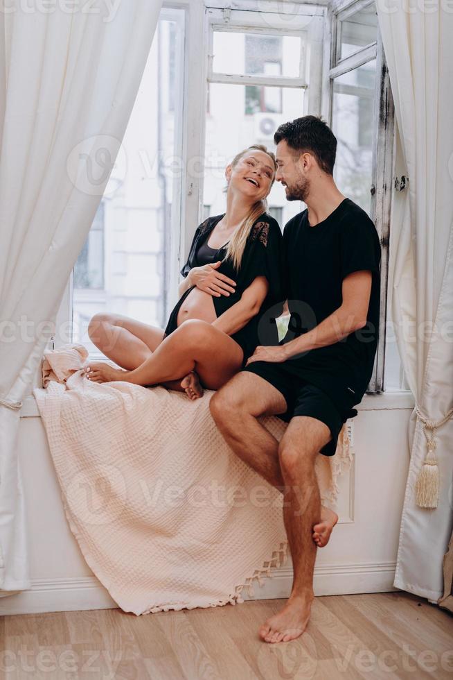 un hombre con una esposa embarazada posando junto a la ventana foto