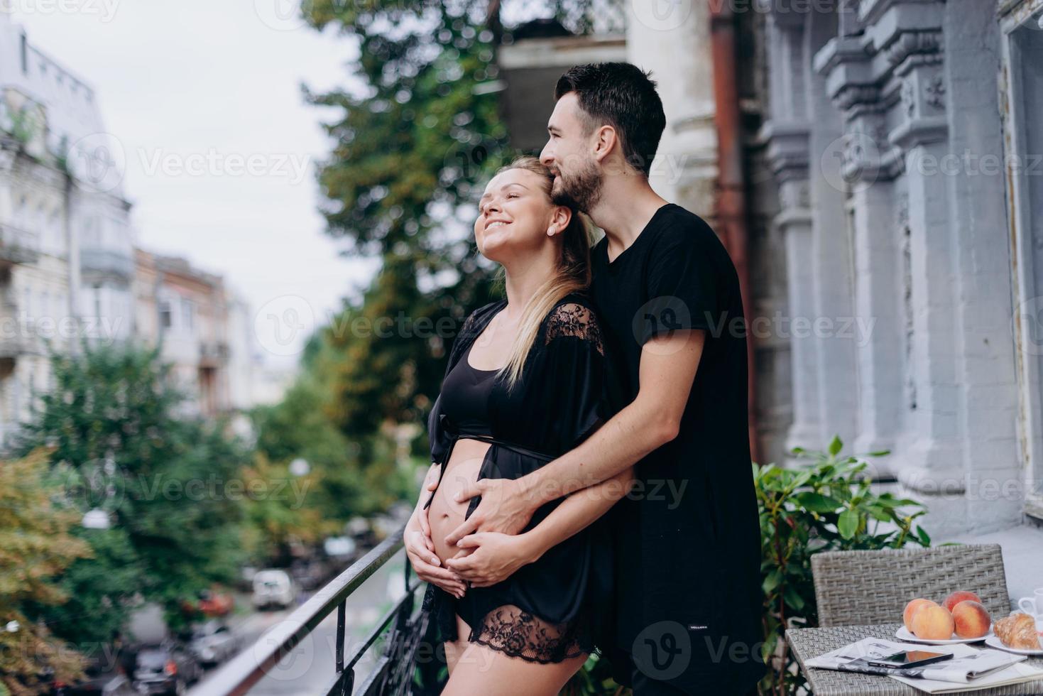 Feliz pareja esperando bebé, en ropa negra posando en la terraza, balcón foto