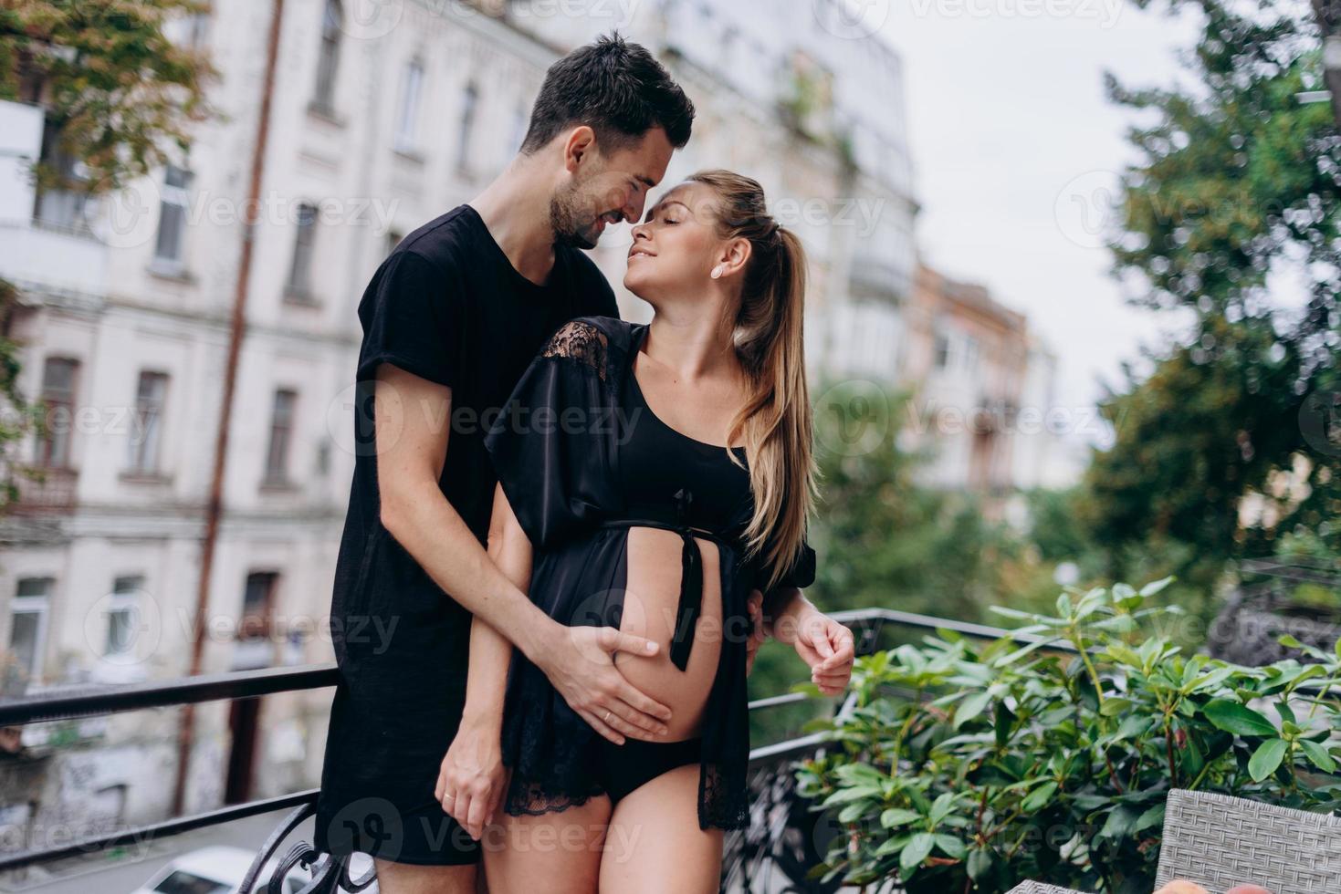 Couple in black clothes posing on balcony waiting for baby photo