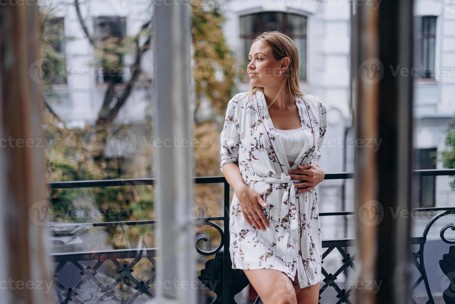 Feliz mujer embarazada en bata de baño abrazando el vientre en la terraza foto