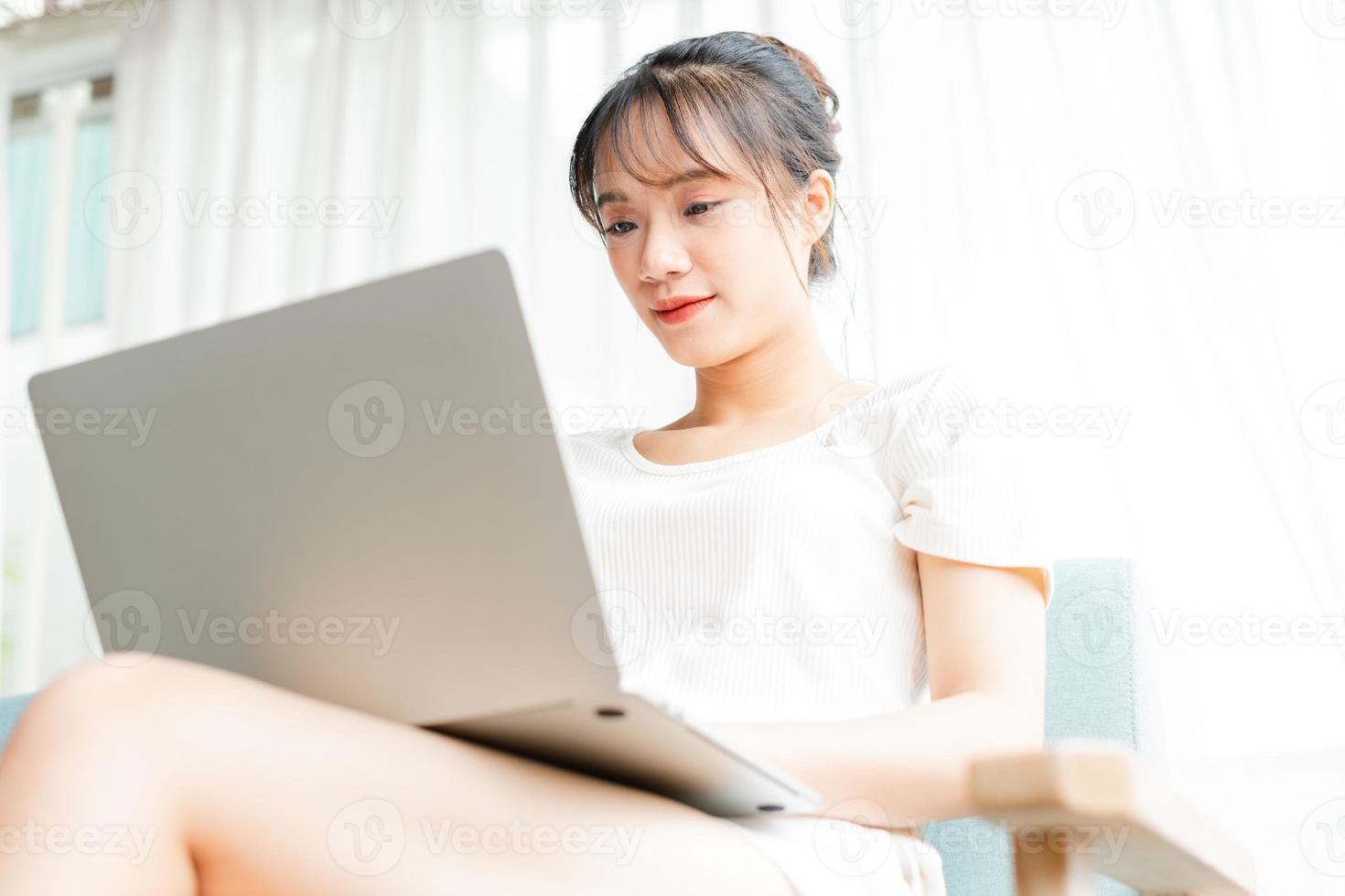 Portrait of young girl sitting on sofa at home using laptop and holding atm card in her hand photo