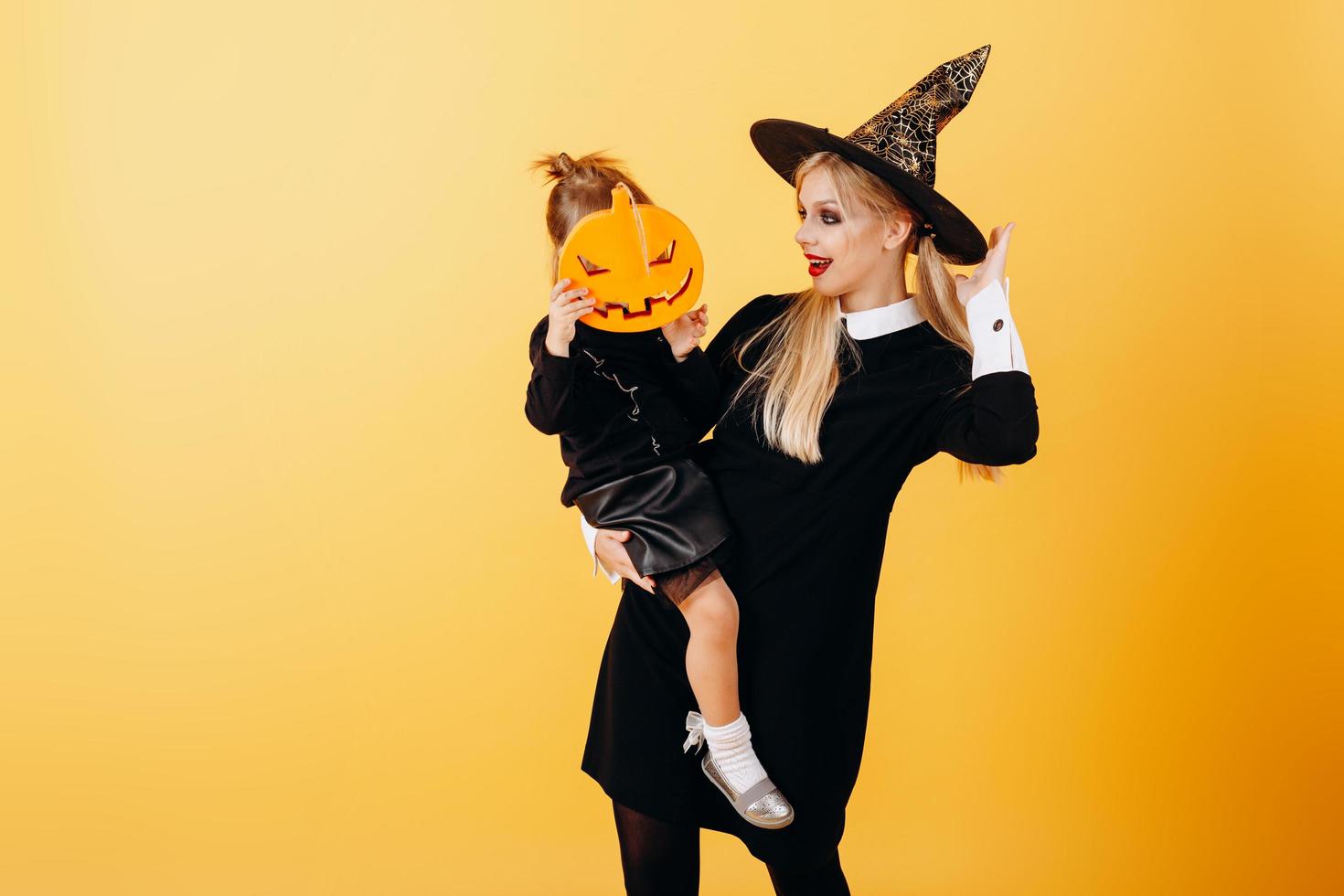 Woman in masquerade dress and hat posing against yellow background holding little girl - Image photo