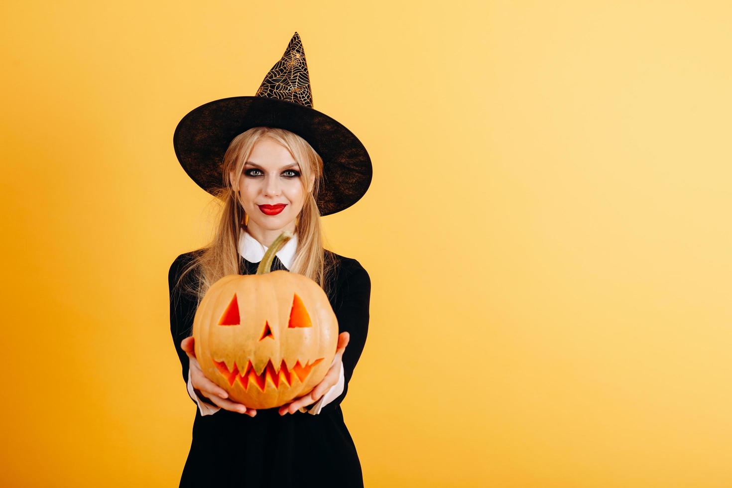 Mujer de pie sobre un fondo amarillo sosteniendo la calabaza y mostrándola con las manos rectas foto