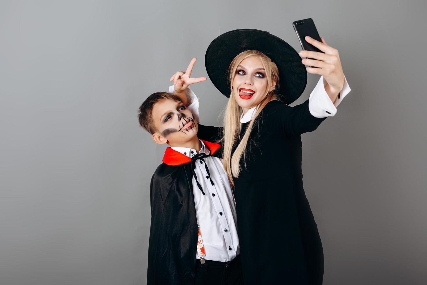 Madre e hijo en disfraces mostrando gesto de victoria y haciendo selfie con fondo de estudio foto