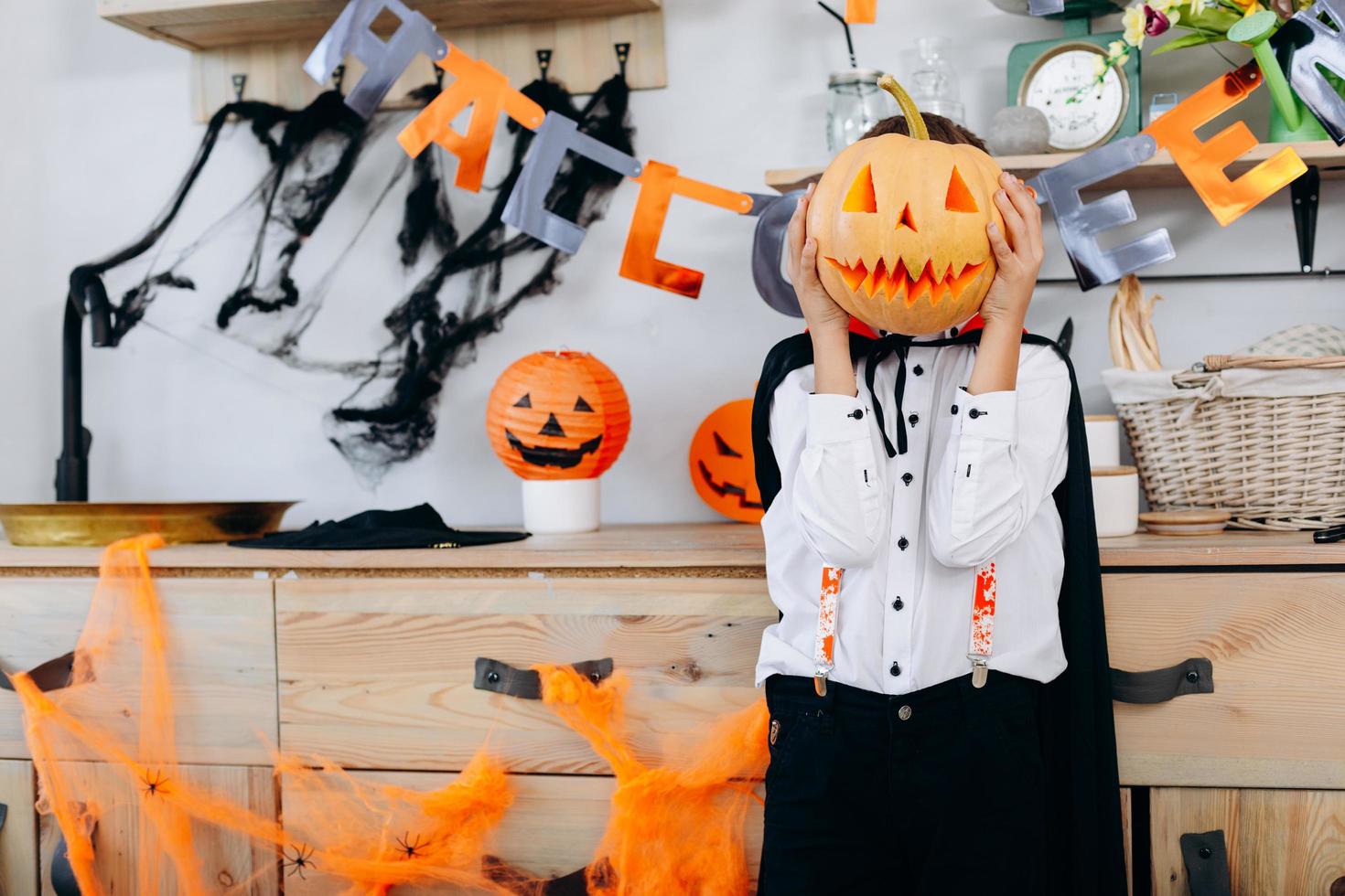 Boy standing  in masquerade  dress holding a pumpkin and hide his face- Image photo