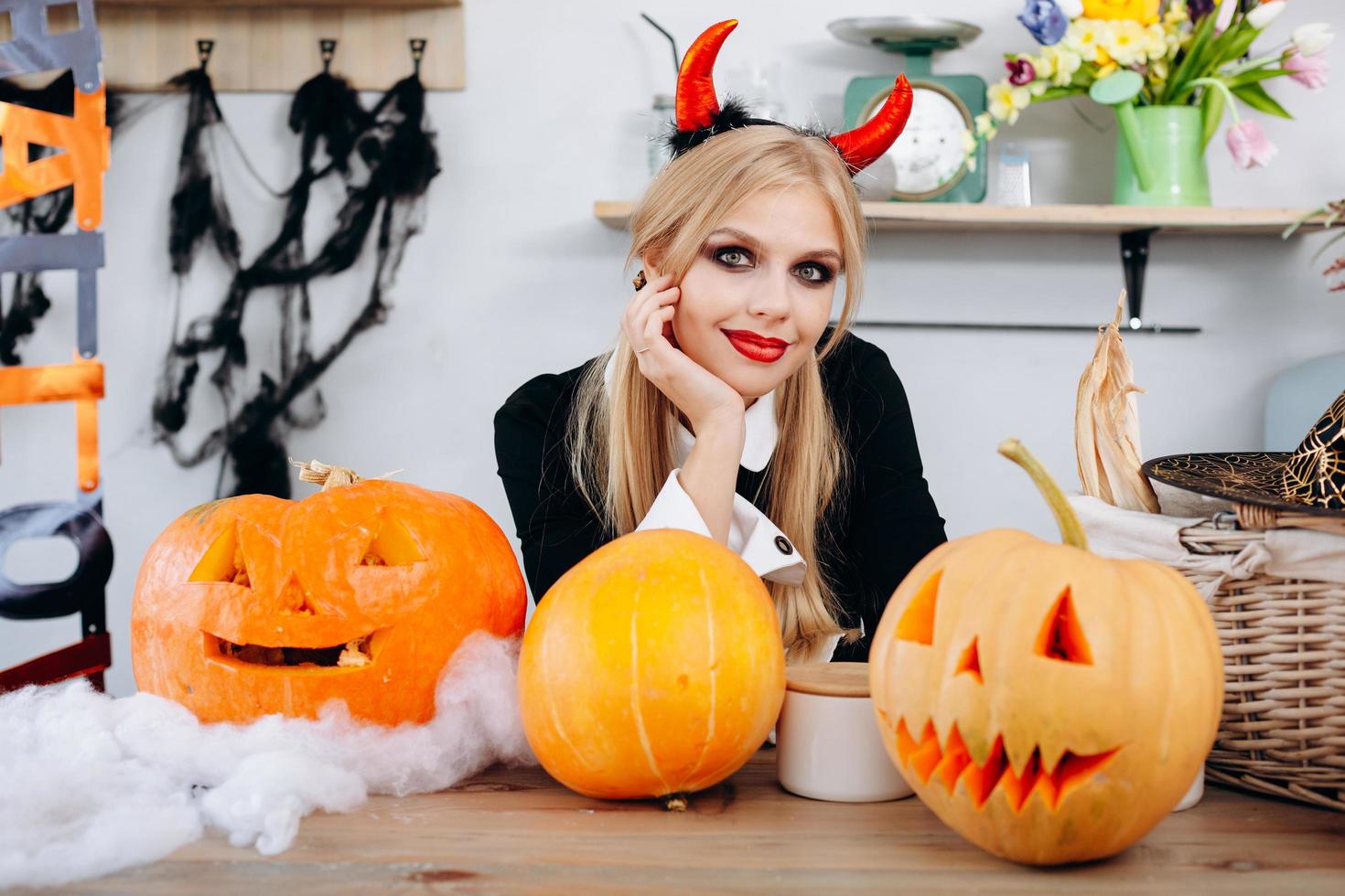 Devil woman sitting at the table next a pumpkins and smiling looking at the camera photo