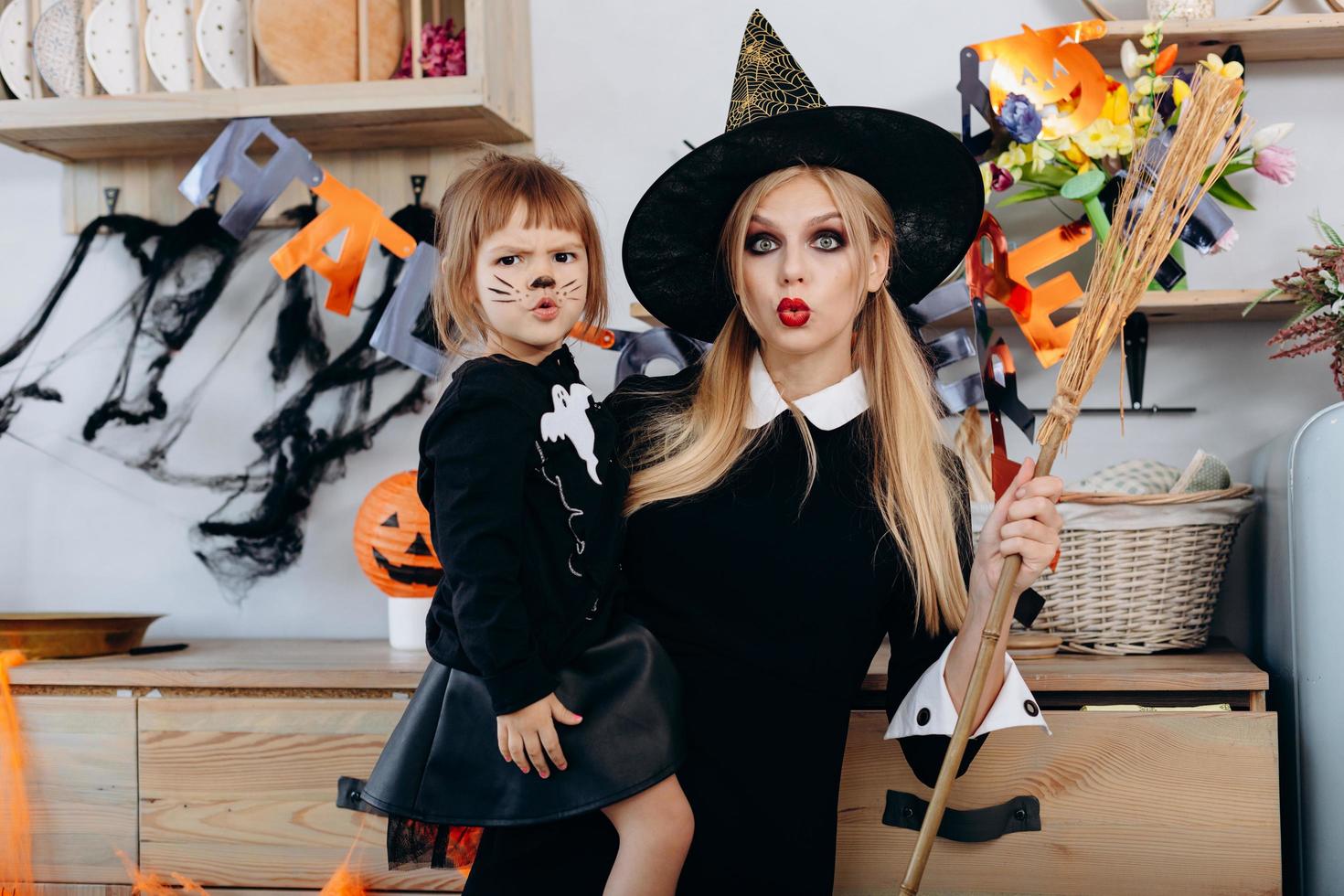 Mother and daughter make scary face standing  in fancy dress and looking at the camera. Woman holding a broom photo
