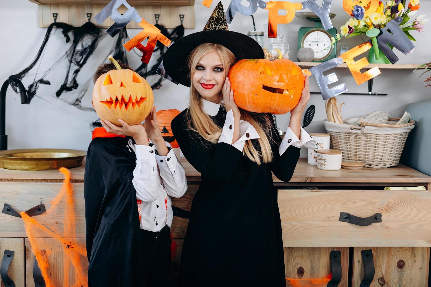 Mother and boy standing in fancy dress holding a pumpkin. Boy hide his ...