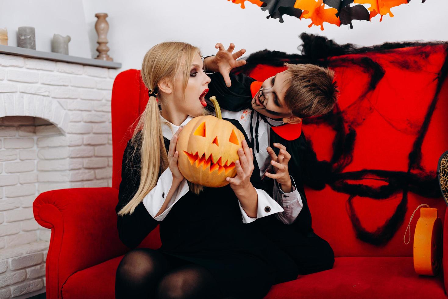 Mother and son have a funny time on red sofa. Boy scary woman.  Halloween concept photo