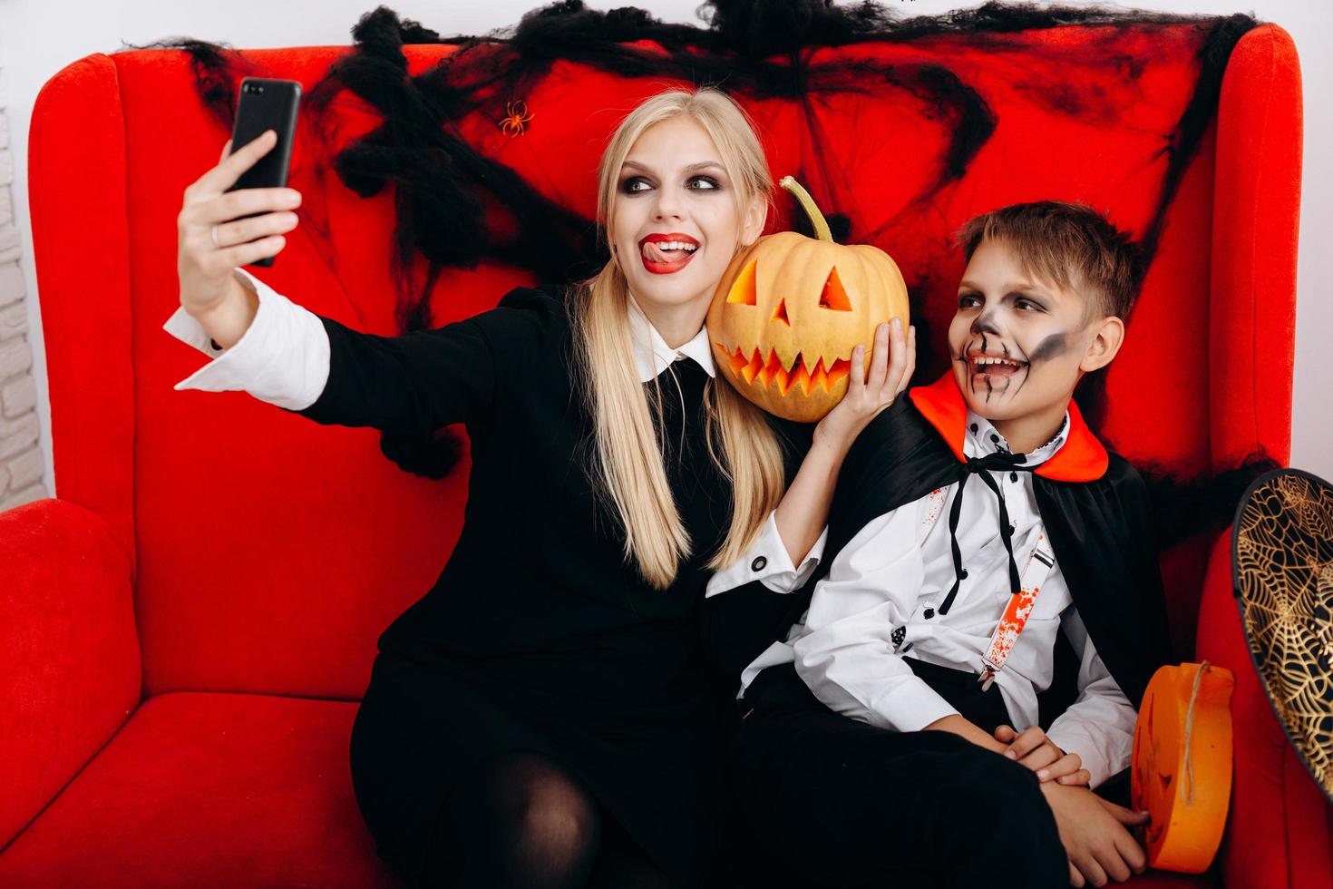 Mother and son have a funny time on red sofa and make a selfie closeup. Emotion and Halloween concept photo