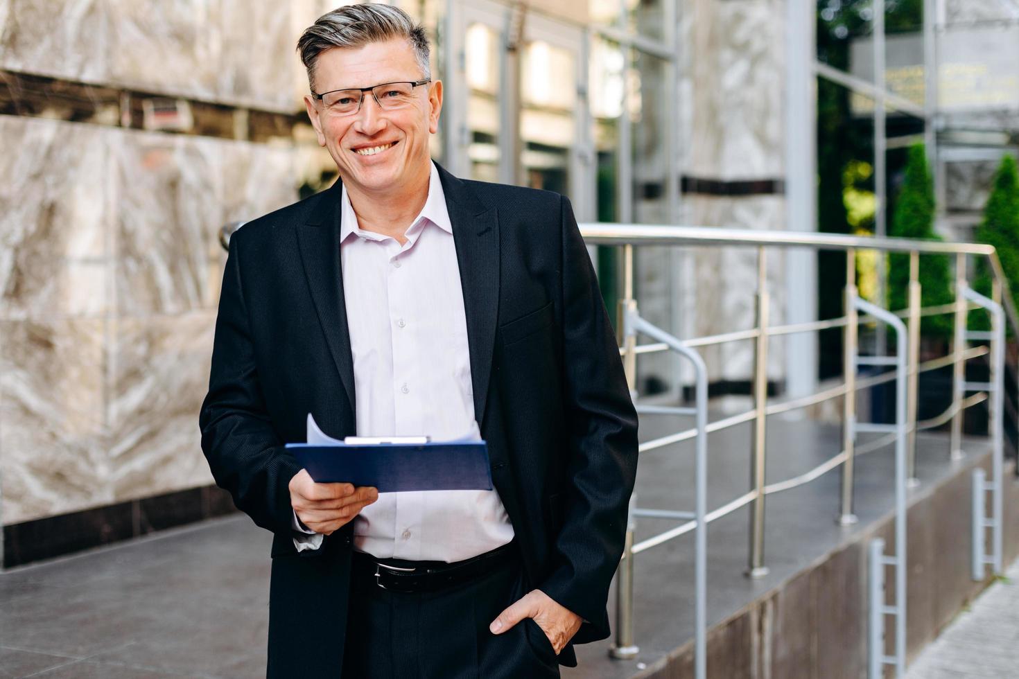 Happy senior businessman in glasses holding a  document and looking at the camera - Image photo