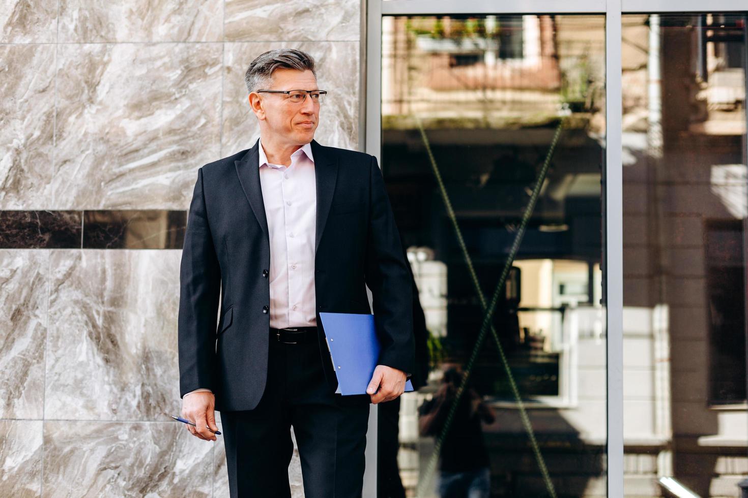 Retrato de hombre mayor serio en traje de pie y sosteniendo un papel al aire libre. - imagen foto