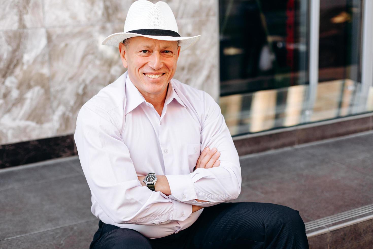 Retrato de hombre mayor en camisa y sombrero sentado en el pavimento con las manos juntas. - imagen foto