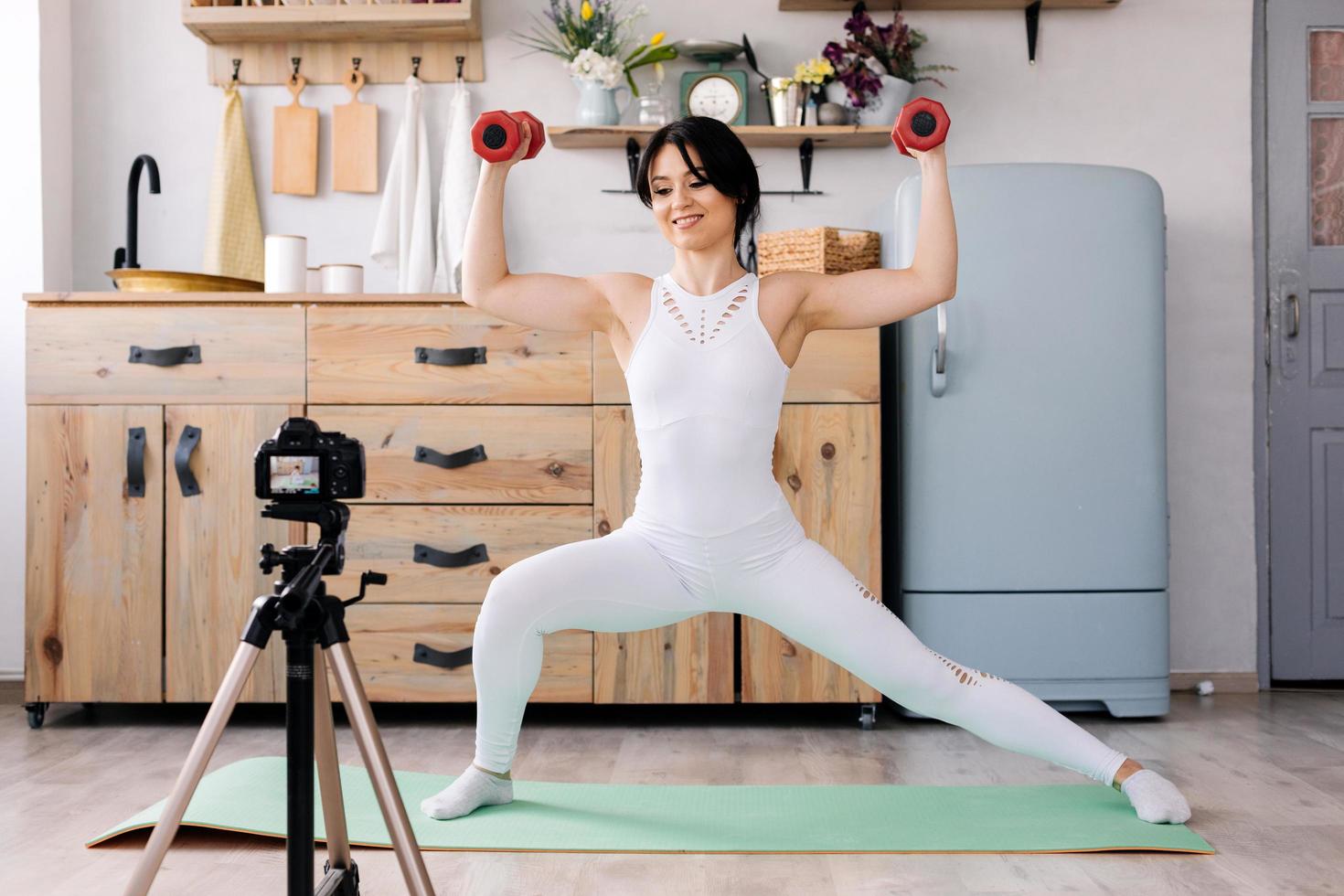 Online training. Joyful young woman making exercises while recording a video of a training photo