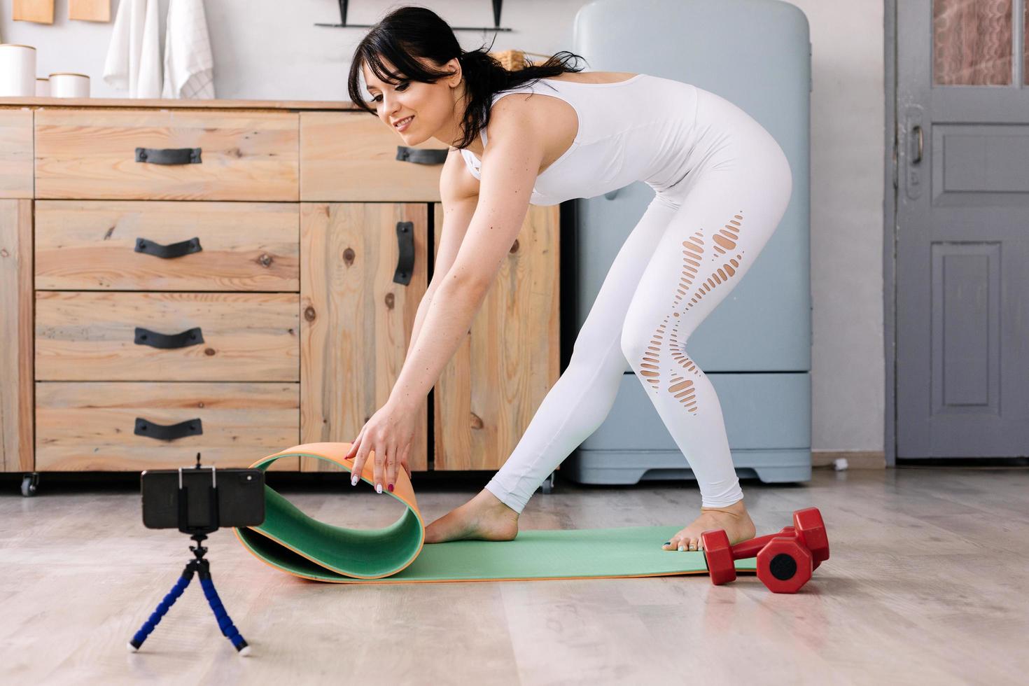 chica deportiva pone una colchoneta de gimnasia y mancuernas foto