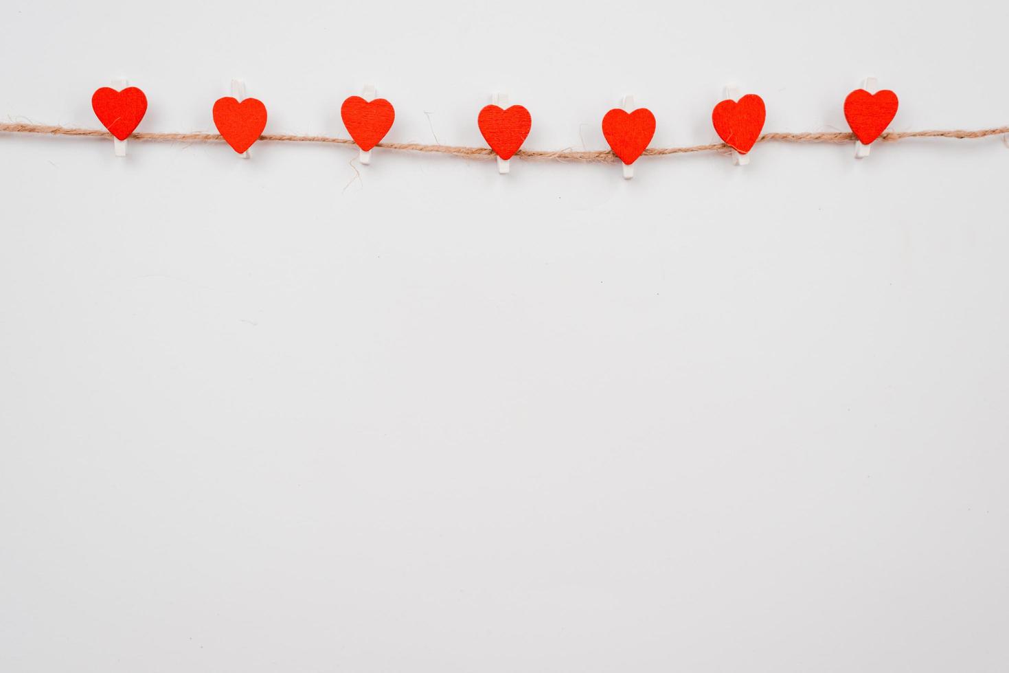 Red paper heart hanging on the clothesline on white wall. Place for advertising photo
