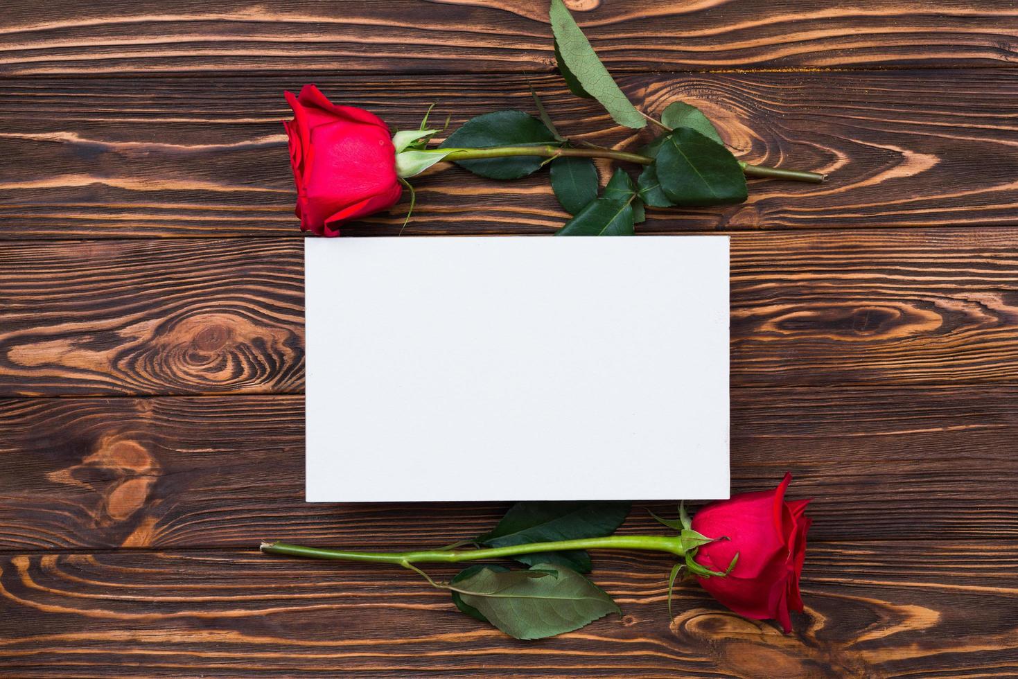 Rosas rojas y trozo de papel en blanco sobre tabla de madera, fondo del día de San Valentín, día de la boda foto