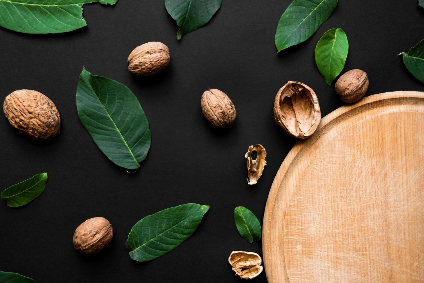 Closeup nutshell and fresh green leafs  on a black background. Part of wooden cutting board photo