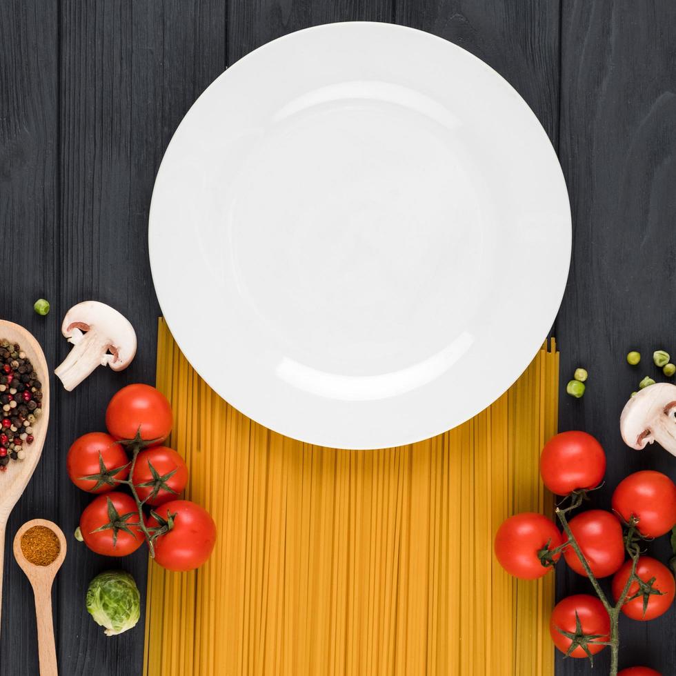 On a dark background stands a plate, pasta, tomatoes, spices photo