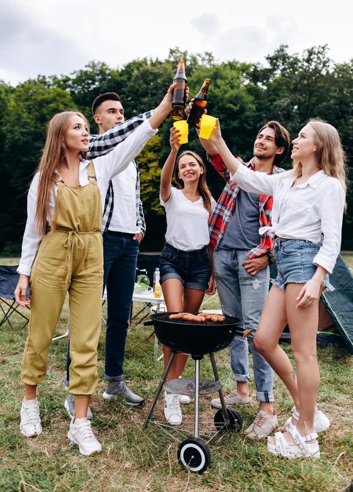 A company of friends raising a bottles with a beer in the camping . - Vertical image photo