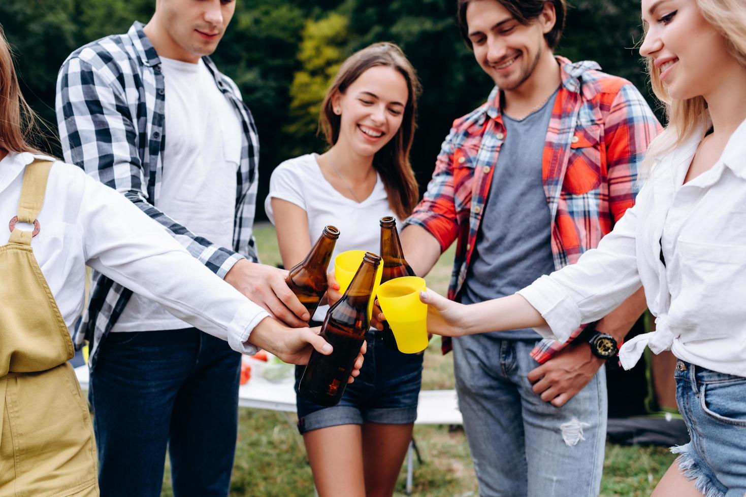 Primer plano de la imagen de una empresa de amigos levantando botellas con una cerveza en el camping foto