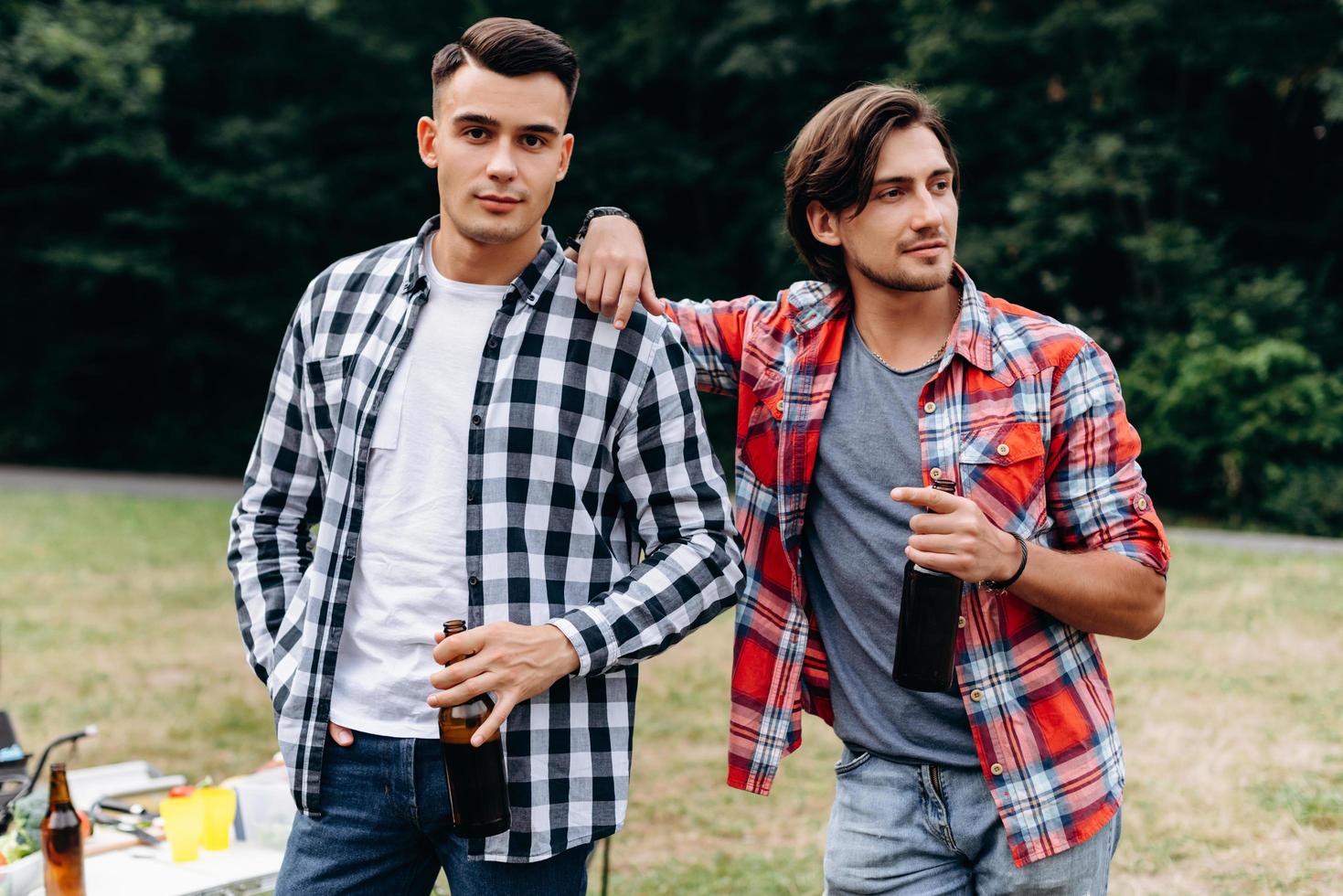 Two guys holding a beer and standing in the camping . - Image photo